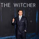 Henry Cavill stands in front of a sign for The Witcher at a red carpet event.